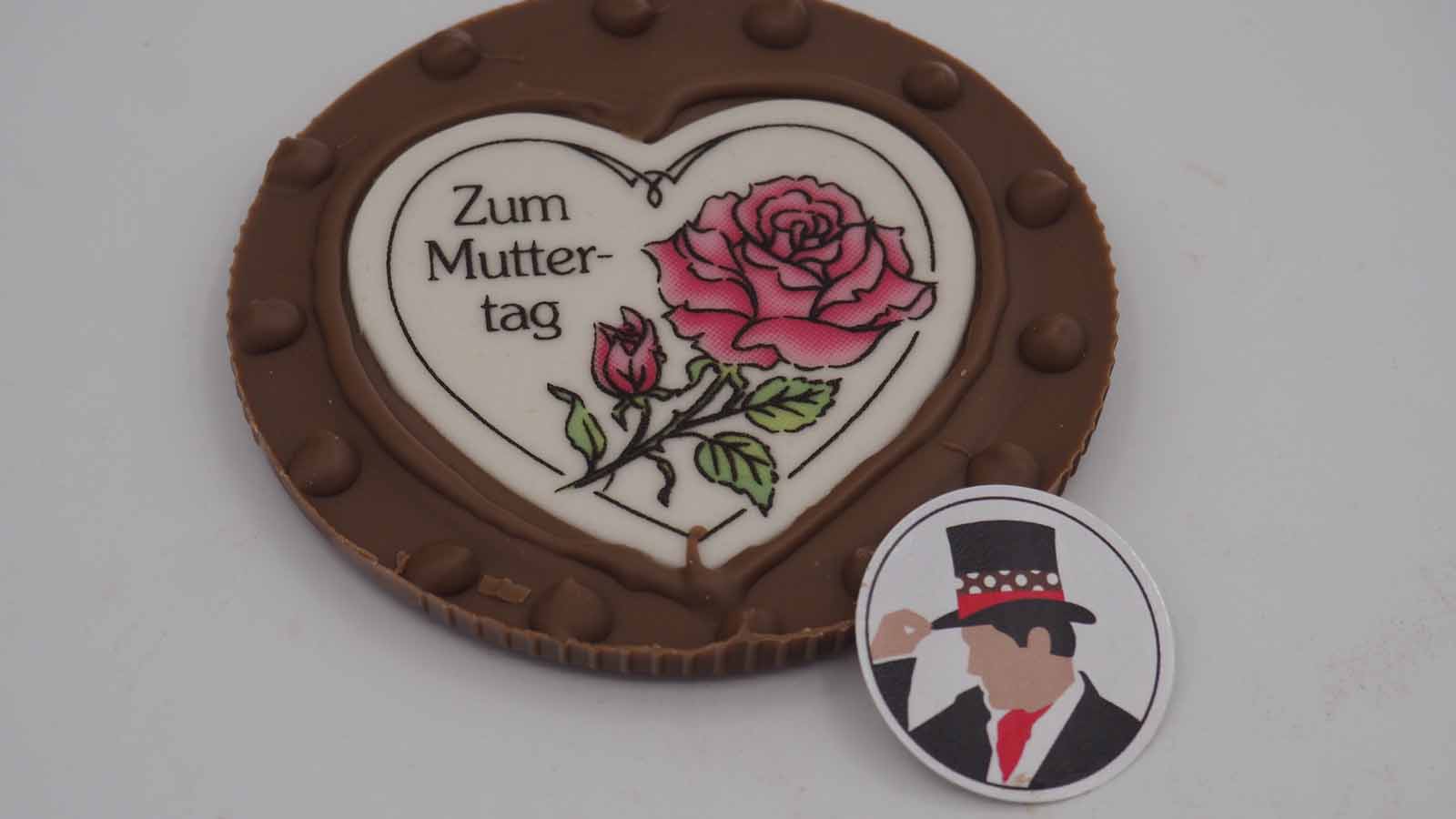 Handgezogene Scheibe aus Vollmilchschokolade mit Dekormasse (rosa Rose, Schriftzug: »Zum Muttertag«) zum Muttertag.