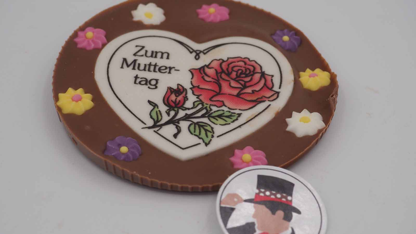 Schokomichi Scheibe aus Vollmilchschokolade mit Dekormasse und Zuckerblümchen zum Muttertag Handgezogene Scheibe aus Vollmilchschokolade mit Dekormasse und Zuckerblümchen zum Muttertag.