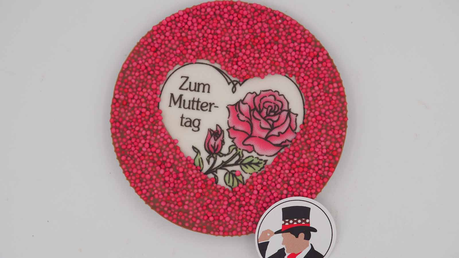 Handgezogene Scheibe aus Vollmilchschokolade mit Dekormasse (rosa Rose, Schriftzug: »Zum Muttertag«) und Nonpareille zum Muttertag.