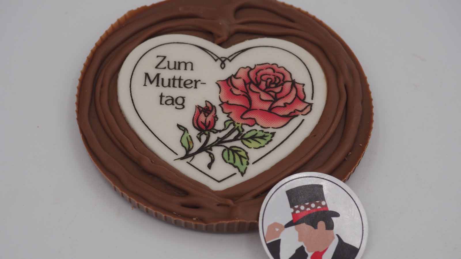 Handgezogene Scheibe aus Vollmilchschokolade mit Dekormasse (rosa Rose, Schriftzug: »Zum Muttertag«) zum Muttertag.