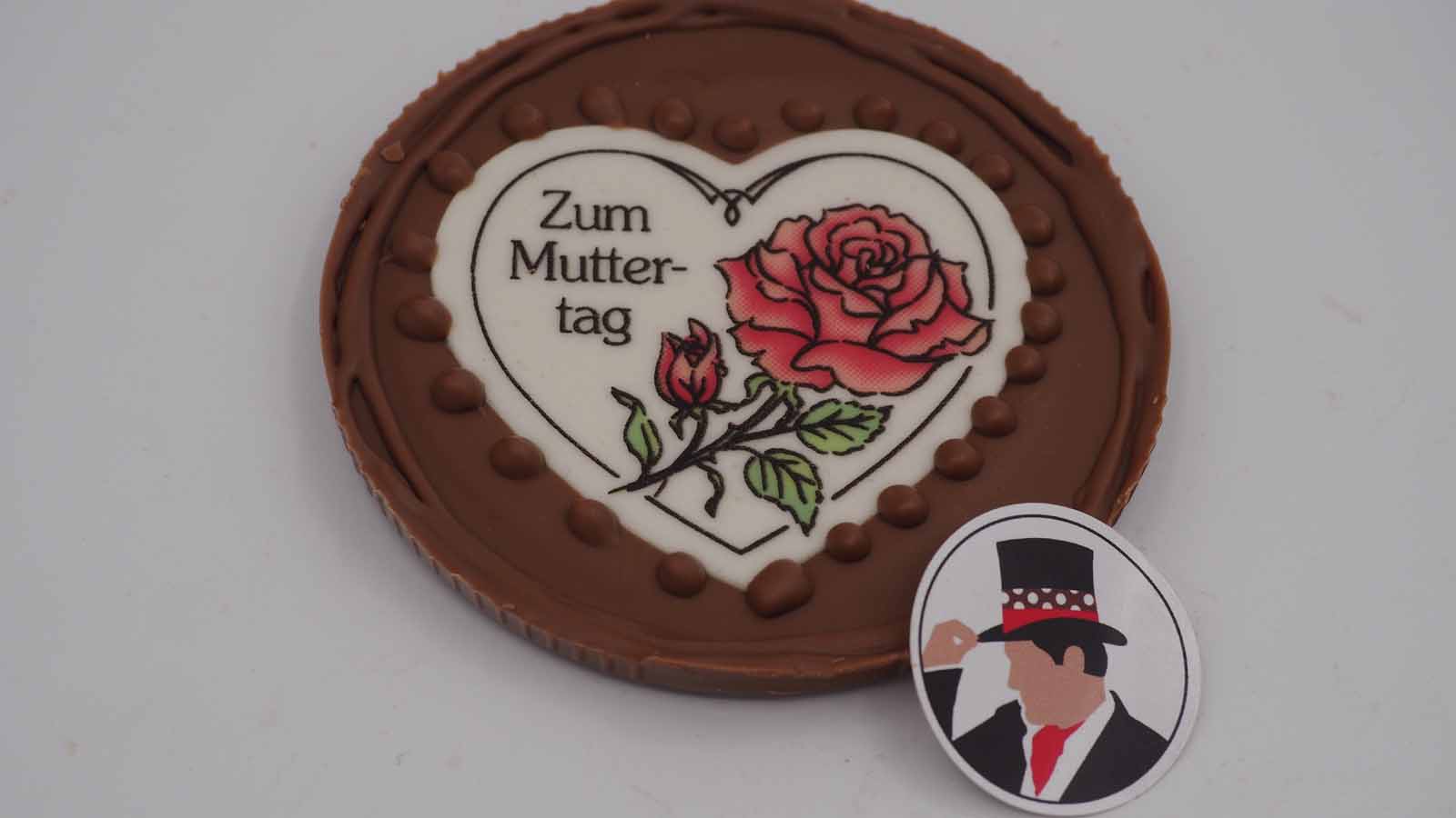 Schokomichi Scheibe aus Vollmilchschokolade mit Dekormasse zum Muttertag Handgezogene Scheibe aus Vollmilchschokolade mit Dekormasse (rosa Rose, Schriftzug: »Zum Muttertag«) zum Muttertag.